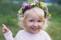 Portraite of small pretty smiling girl with blond curly hair and blue eyes wearing wild flowers wreath Royalty Free Stock Photo