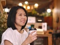 Portraits of Asian woman holding a cup of coffee looking to her left hand in cozy coffee shop. Royalty Free Stock Photo