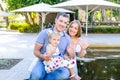 Portraits of happy family of three -mother, father and daughter waving their hands at the camera sitting near pond in the park. Fa Royalty Free Stock Photo