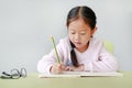 Portraits of little Asian child girl write in a book or notebook with pencil sitting on kid chair and table against white Royalty Free Stock Photo