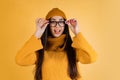 Cropped portrat of young excited woman touching glasses, wearing colorful sweater over yellow background