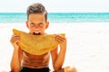 Portreit of handsome hipster teen boy holding, eating meat pasty on the beach. Caucasian, Cheburek