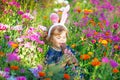 Portriat of adorable, charming toddler girl with Easter bunny ears eating chocolate bunny figure in flowers meadow