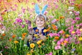 Portriat of adorable, charming toddler girl with Easter bunny ears eating chocolate bunny figure in flowers meadow