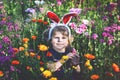 Portriat of adorable, charming toddler girl with Easter bunny ears eating chocolate bunny figure in flowers meadow