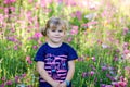 Portriat of adorable, charming toddler girl in flowers meadow. Smiling happy baby child on summer day with colorful
