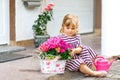 Portriat of adorable, charming toddler girl sitting by house with flowers. Smiling happy baby child on summer day with