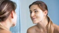 Portriat of beautiful young woman looking at her face in mirror