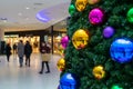 Christmas shoppers walking past a christmas tree decorated with bright baubles in a shopping