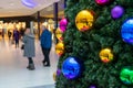 Christmas shoppers walking past a christmas tree decorated with bright baubles in a shopping