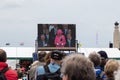 A crowd watching a big screen as queen Elizabeth addresses them