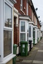 The exterior of typical english brick terraced houses with green wheelie bins at the front