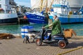 A middle aged man on a mobility scooter taking his dog for a walk on the quayside or dock