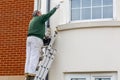 10/20/2020 Portsmouth, Hampshire, UK A painter at the top of a ladder painting the side of a house with a paint roller