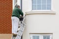 10/20/2020 Portsmouth, Hampshire, UK A painter at the top of a ladder painting the side of a house