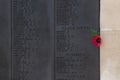 A single red poppy on a war memorial next to the roll of honor