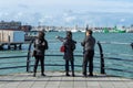 Three Asian tourists looking out to sea at the view pointing at boats