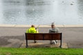 Two men in work clothing sitting on a park bench in front of a lake