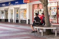 Two teenage boys sat on a bench in a high street