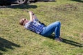 A woman laid alone on a grass verge in the sunshine looking at her mobile phone or cell phone Royalty Free Stock Photo