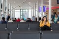 A young woman looking at her phone with headphones in smiling while seated waiting a a