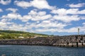 PPortugal, San Miguel, June 2019. White fluffy clouds in the blue sky, lighthouse and marina of Vila Franca do Campo, Azores.