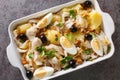 Portuguese Bacalhau a Gomes de Sa salted cod baked with potatoes, onions served with eggs and olives close-up in a baking dish.