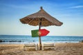 Portuguese flag on wooden arrow sign. There are two sun loungers and a sun umbrella on the beach. It is a tropical paradise with a