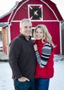 Posed portrait of a attractive mature couple outdoors by a red barn during the Christmas season. Happy Holidays Royalty Free Stock Photo