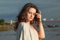 Posing brunette woman with fresh skin, natural make-up and healthy wavy brown hair enjoying the sunny morning and sea air. Female Royalty Free Stock Photo