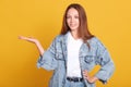 Positive adorable female with dark satraight hiar, keeps palm raised up, demonstrates spmething, being in high spirit, posing Royalty Free Stock Photo