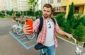Positive adult man with a beard stands with a bicycle on the street and takes a selfie with a smile on the face of the cyclist.