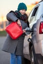 Positive adult woman a driver pouring petrol from red plastic gasoline can into a car tank on the road Royalty Free Stock Photo