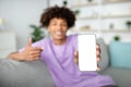 Positive African American adolescent pointing at smartphone with mockup for mobile app on screen, selective focus