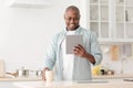 Positive african american mature man reading news on digital tablet and drinking coffee in kitchen Royalty Free Stock Photo
