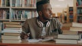 Positive african american young handsome guy with big headphones is sitting at table with books, looking through window Royalty Free Stock Photo