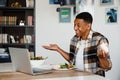 Positive african man having video call via laptop and gesturing while having lunch Royalty Free Stock Photo