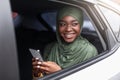Positive african muslim lady using smartphone while having road trip in car