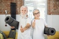 Positive aged couple showing thumb up and holding yoga mat