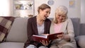 Positive aged ladies looking album photos sitting sofa at home, cheerful friends