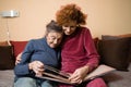 Positive aged ladies looking album photos sitting sofa at home, cheerful friends. Senior woman and her mature nurse watching photo