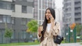 Positive amiable black woman talking on phone and drinking coffee in city