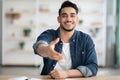 Positive arab man in casual sitting at workdesk, giving hand