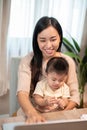 A positive Asian mom is taking care of her baby boy while working on her laptop computer Royalty Free Stock Photo