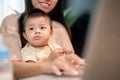 A positive Asian mom is taking care of her baby boy while working on her laptop computer Royalty Free Stock Photo