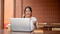 A positive Asian woman is talking on the phone with her client while working remotely at a cafe Royalty Free Stock Photo