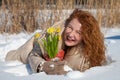 Full length of pleased woman lying on snow surface with yellow narcissuses
