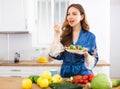 Young woman in blue silk robe enjoying vegetable salad in kitchen Royalty Free Stock Photo