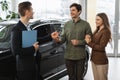 Positive auto showroom manager giving car key to happy young clients at car dealership Royalty Free Stock Photo