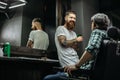 Positive bearded barber looking at his client and smiling Royalty Free Stock Photo